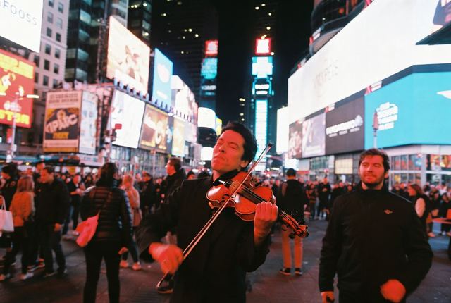 7:10 PM • Times Square — Neon Violin: A passionate street violinist plays with eyes closed in the heart of Times Square as neon lights explode around him.